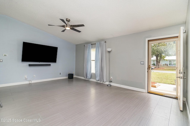 unfurnished living room with ceiling fan, vaulted ceiling, a textured ceiling, and a wealth of natural light