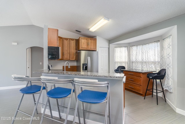 kitchen with stainless steel refrigerator with ice dispenser, sink, a breakfast bar area, vaulted ceiling, and stone counters