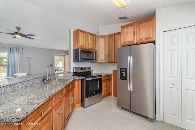 kitchen featuring sink, ceiling fan, stainless steel appliances, light stone countertops, and a textured ceiling