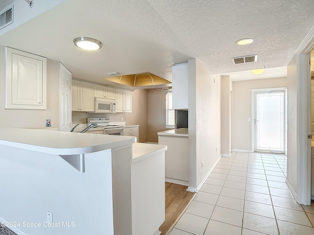 kitchen with a breakfast bar area, kitchen peninsula, white cabinetry, and white appliances