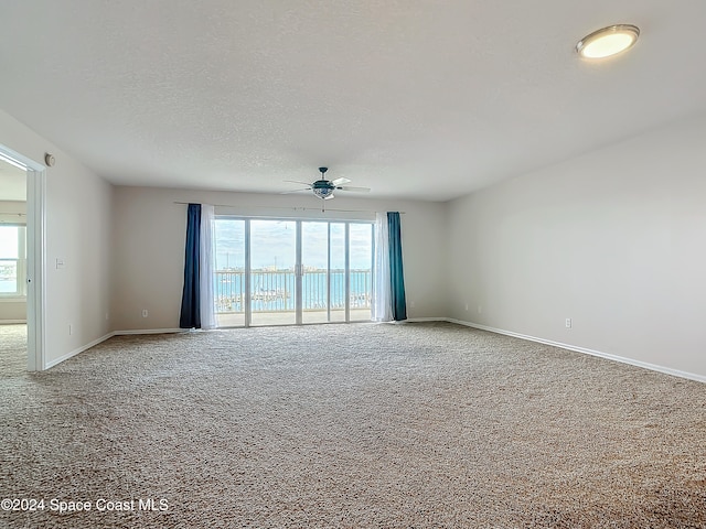 carpeted empty room featuring a textured ceiling, a wealth of natural light, and ceiling fan