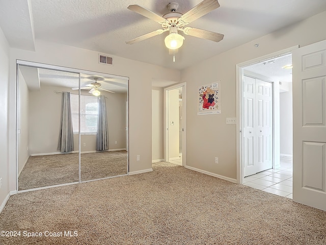 unfurnished bedroom with light carpet, a textured ceiling, a closet, and ceiling fan