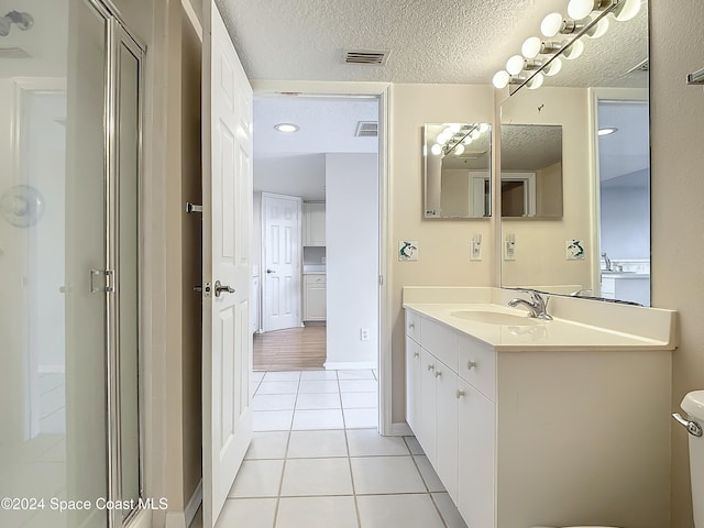 bathroom featuring tile patterned floors, vanity, a shower with door, and a textured ceiling