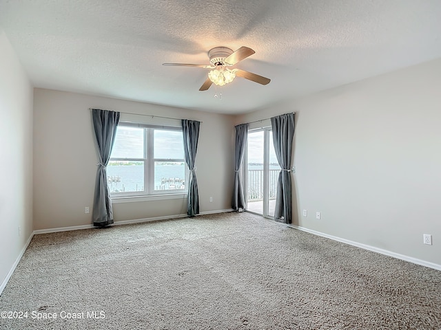 unfurnished room featuring carpet, a textured ceiling, a water view, and ceiling fan