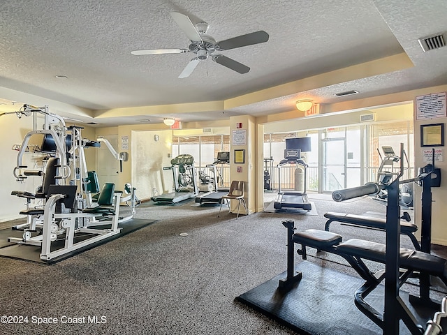 gym with ceiling fan, a textured ceiling, and a tray ceiling