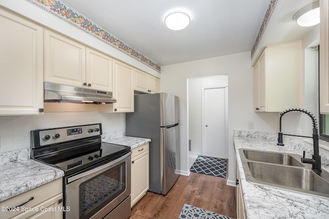 kitchen featuring dark wood-type flooring, cream cabinets, sink, appliances with stainless steel finishes, and light stone counters