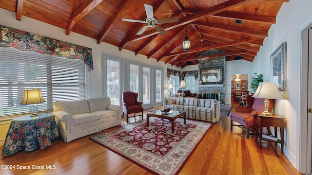 living room with lofted ceiling with beams, ceiling fan, light wood-type flooring, a fireplace, and wood ceiling