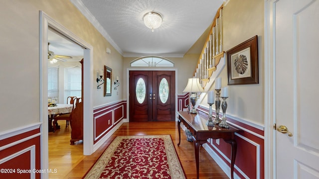 foyer featuring hardwood / wood-style floors, french doors, ceiling fan, ornamental molding, and a textured ceiling