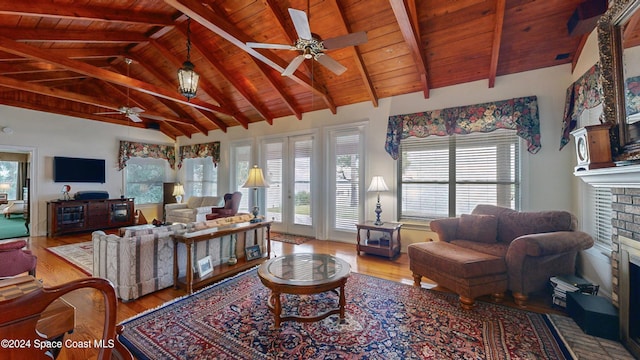 living room featuring vaulted ceiling with beams, ceiling fan, light wood-type flooring, and a fireplace