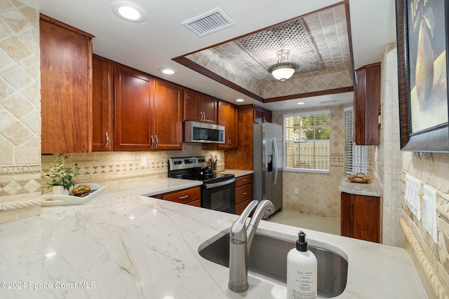 kitchen with sink, light stone countertops, appliances with stainless steel finishes, a tray ceiling, and kitchen peninsula