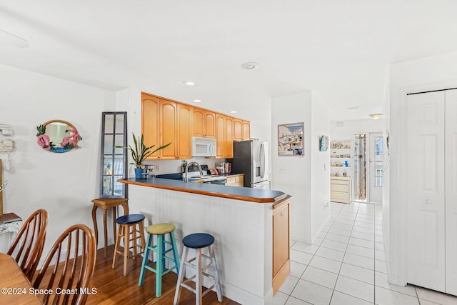 550 S Brevard Ave Unit 523, Cocoa Beach, FL 32931 - kitchen featuring white microwave, stainless steel fridge with ice dispenser, stove, baseboards, and a breakfast bar area