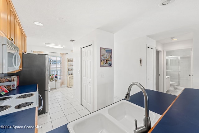 kitchen with light tile patterned floors, white appliances, sink, and light brown cabinetry