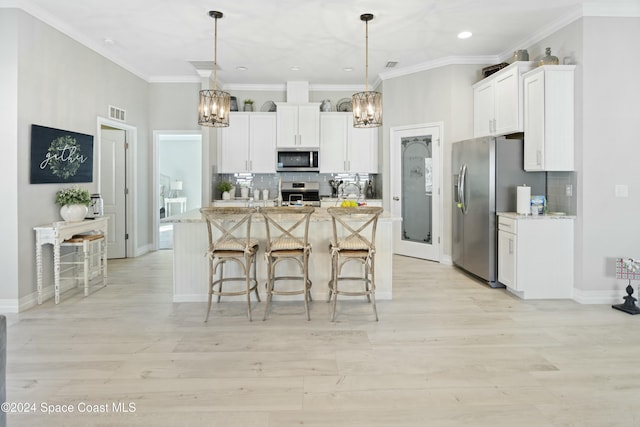 kitchen with hanging light fixtures, white cabinetry, a center island with sink, and stainless steel appliances