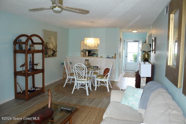 living room featuring hardwood / wood-style floors, ceiling fan with notable chandelier, and a textured ceiling