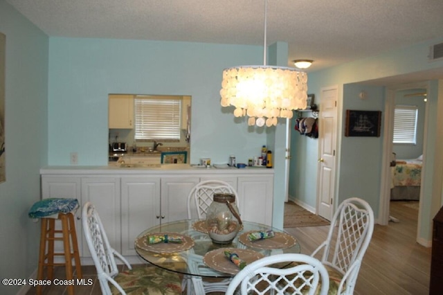 dining area featuring a textured ceiling, light wood-type flooring, a notable chandelier, and sink