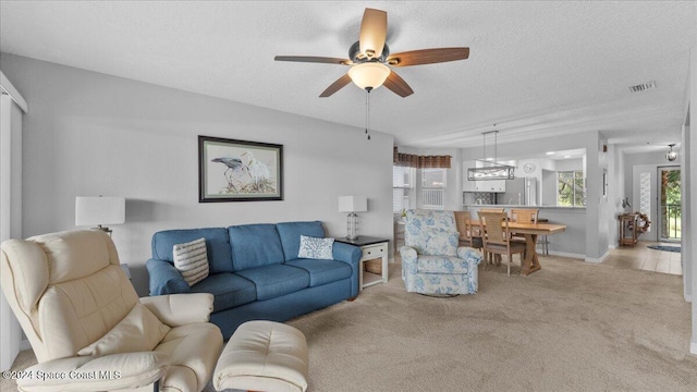 living room with plenty of natural light, ceiling fan, light colored carpet, and a textured ceiling