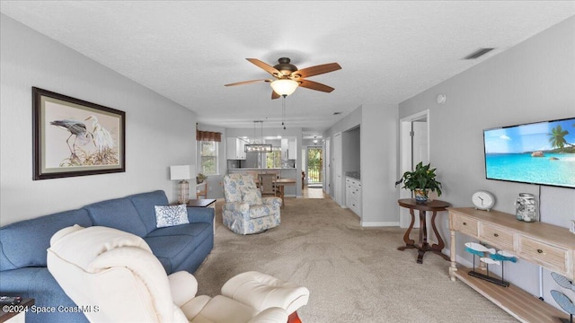 living room featuring light carpet, ceiling fan, and a textured ceiling