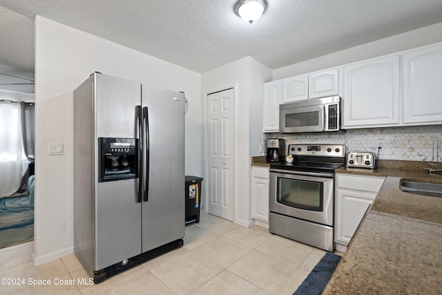 kitchen with decorative backsplash, light tile patterned floors, white cabinetry, and appliances with stainless steel finishes