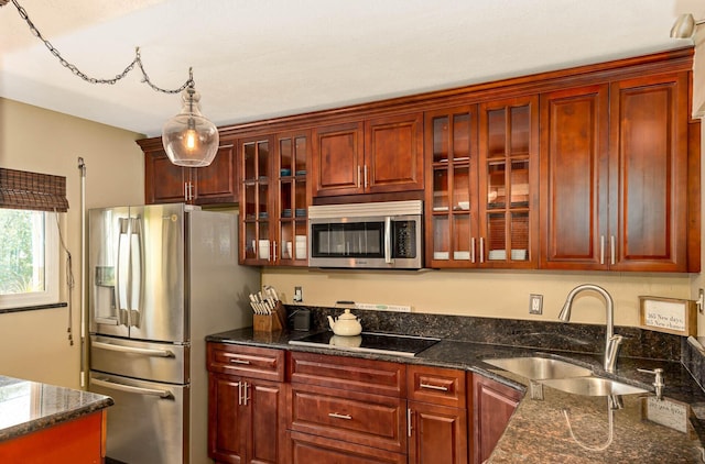 kitchen featuring stainless steel appliances, hanging light fixtures, dark stone counters, and sink