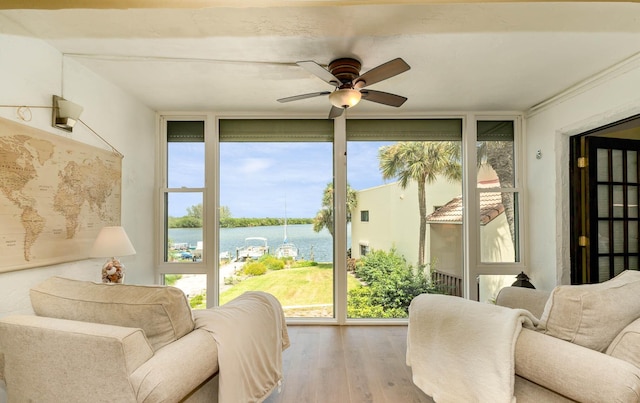 sunroom with ceiling fan and a water view