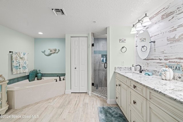 bathroom with hardwood / wood-style floors, vanity, independent shower and bath, and a textured ceiling