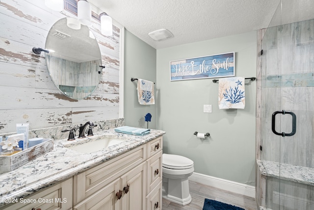 bathroom with vanity, a shower with door, toilet, a textured ceiling, and wood-type flooring