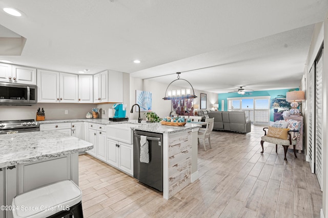 kitchen featuring appliances with stainless steel finishes, light stone counters, sink, light hardwood / wood-style flooring, and hanging light fixtures