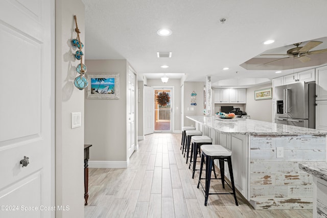 kitchen with light stone counters, high end fridge, a breakfast bar, light hardwood / wood-style flooring, and white cabinets