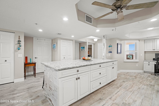 kitchen with ceiling fan, white cabinetry, a kitchen island, and light wood-type flooring