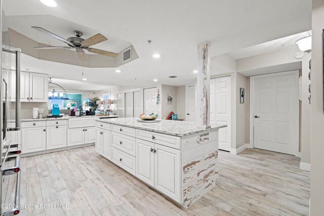 kitchen with light stone countertops, ceiling fan, a kitchen island, light hardwood / wood-style floors, and white cabinets