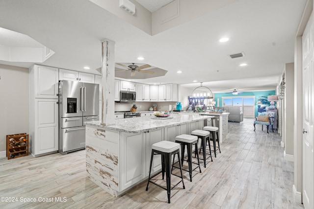 kitchen featuring white cabinetry, light stone counters, light hardwood / wood-style floors, a kitchen bar, and appliances with stainless steel finishes