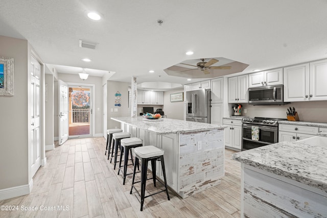 kitchen featuring a center island, light hardwood / wood-style floors, light stone counters, white cabinetry, and stainless steel appliances