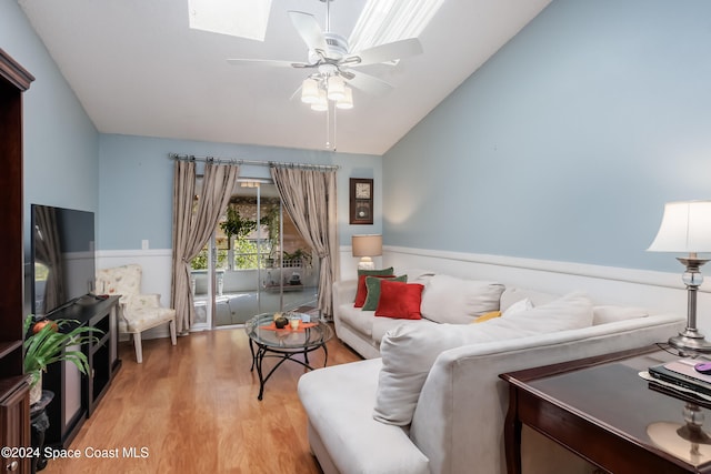 living room with vaulted ceiling with skylight, ceiling fan, and light wood-type flooring