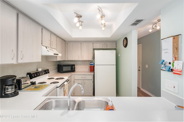 kitchen with a tray ceiling, decorative backsplash, sink, and white appliances