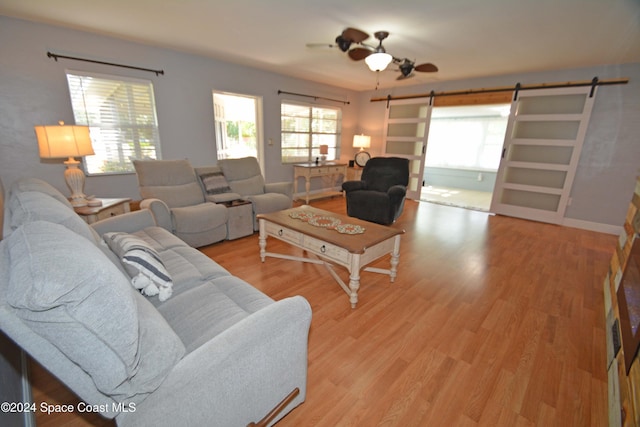 living room featuring ceiling fan, a barn door, and light hardwood / wood-style flooring