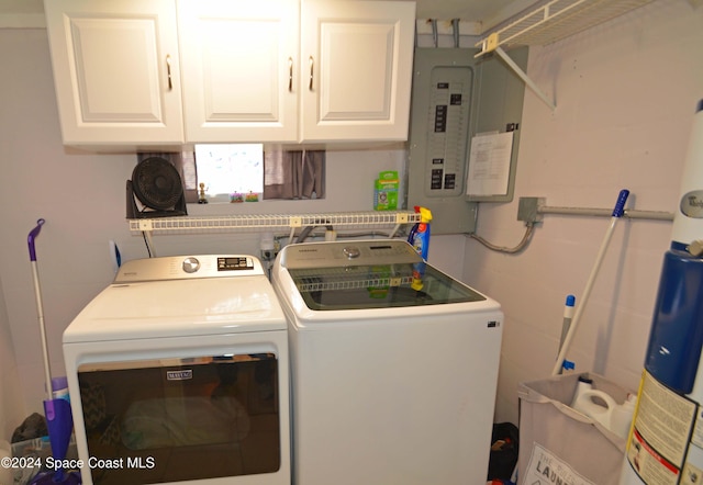 clothes washing area with cabinets, gas water heater, washing machine and dryer, and electric panel