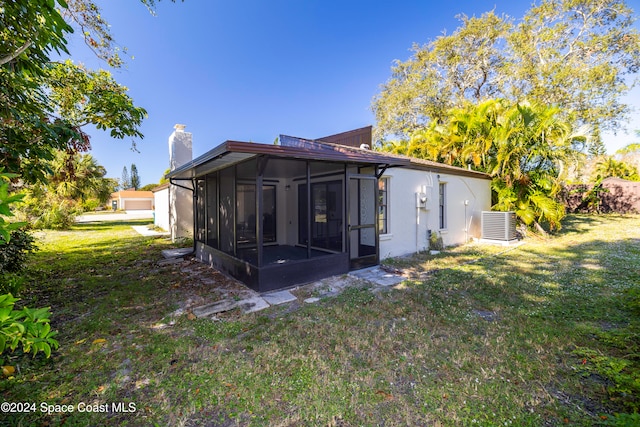 back of property featuring a sunroom, central air condition unit, and a lawn