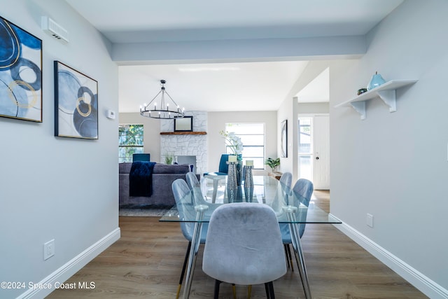 dining space featuring hardwood / wood-style floors, an inviting chandelier, a stone fireplace, and plenty of natural light