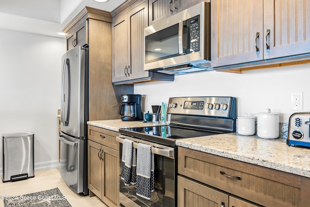 kitchen with light stone countertops, light wood-type flooring, and stainless steel appliances