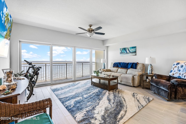 living room featuring ceiling fan, a water view, a textured ceiling, and light wood-type flooring