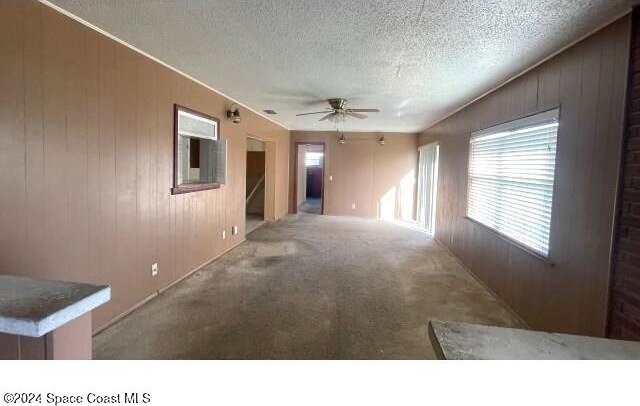 unfurnished room featuring carpet flooring, a textured ceiling, ceiling fan, and wood walls