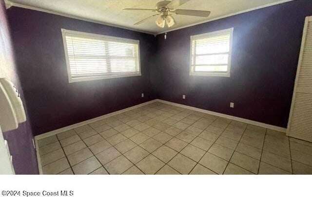 spare room featuring ceiling fan, crown molding, and light tile patterned floors