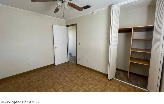 unfurnished bedroom with dark parquet flooring, ceiling fan, a closet, and ornamental molding