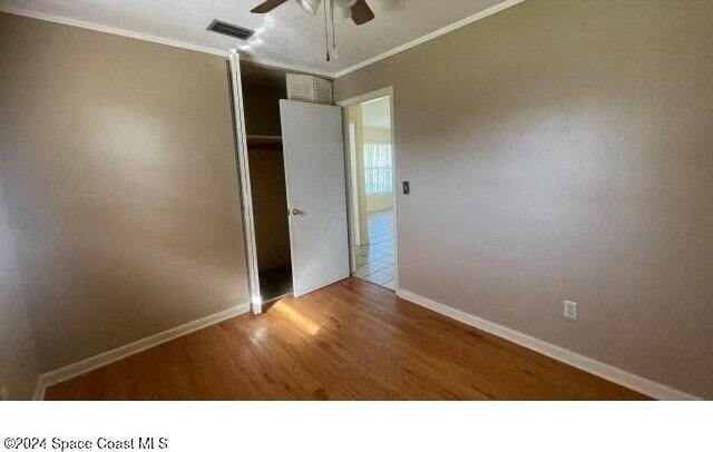 unfurnished bedroom featuring a closet, ceiling fan, crown molding, and wood-type flooring