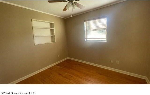 unfurnished room with built in shelves, ceiling fan, wood-type flooring, and ornamental molding