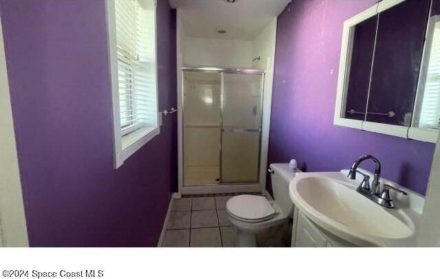 bathroom featuring toilet, tile patterned floors, a shower with door, and sink