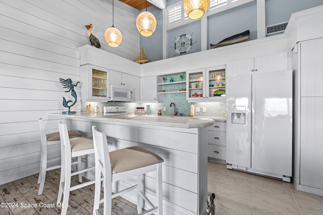 kitchen with pendant lighting, a breakfast bar, white appliances, a towering ceiling, and white cabinetry