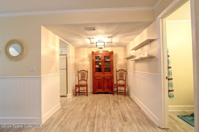 hall with a textured ceiling, light wood-type flooring, and ornamental molding