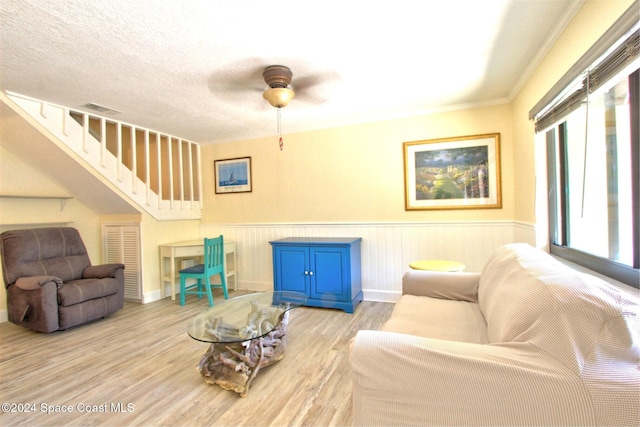 living room with ceiling fan, light hardwood / wood-style flooring, crown molding, and a textured ceiling