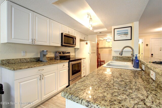 kitchen with a textured ceiling, stainless steel appliances, sink, light hardwood / wood-style floors, and white cabinetry